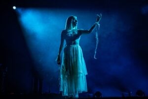 AURORA en vivo, iluminada en azul y con vestido de tul, durante un concierto de la gira What Happened to the Earth?